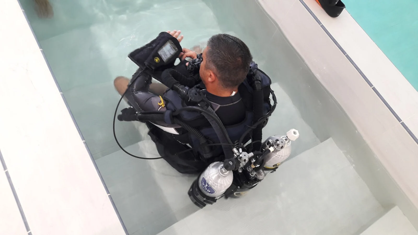 Antonio seated in shallow water with a rebreather, showing the unit, loop and cylinders from above.