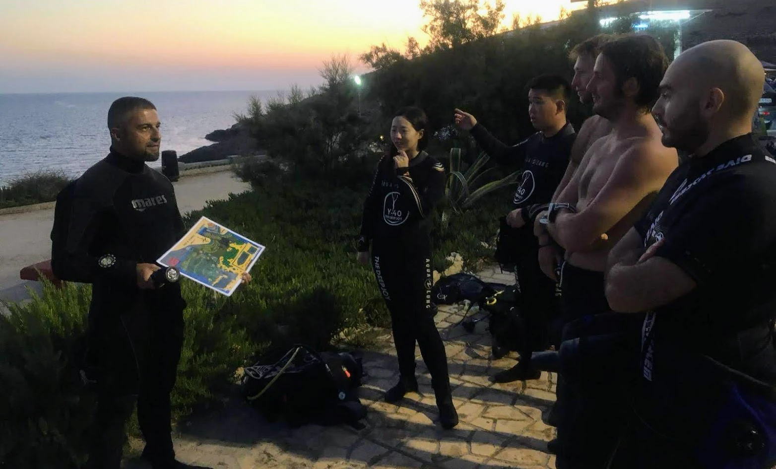 A diving instructor briefing a group of divers at sunset before a shore dive