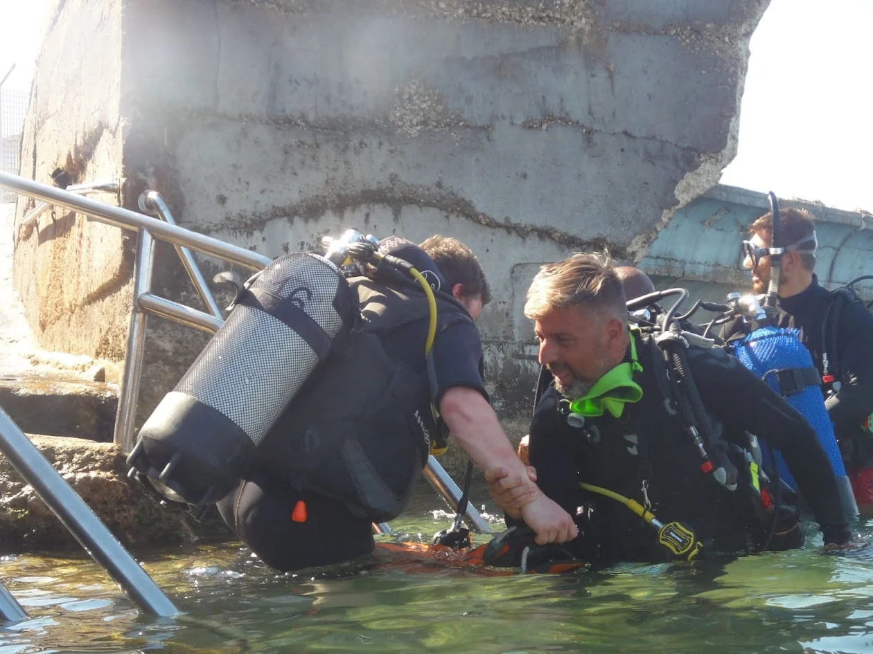 A scuba instructor assisting a student during the first moments of a shore-entry dive